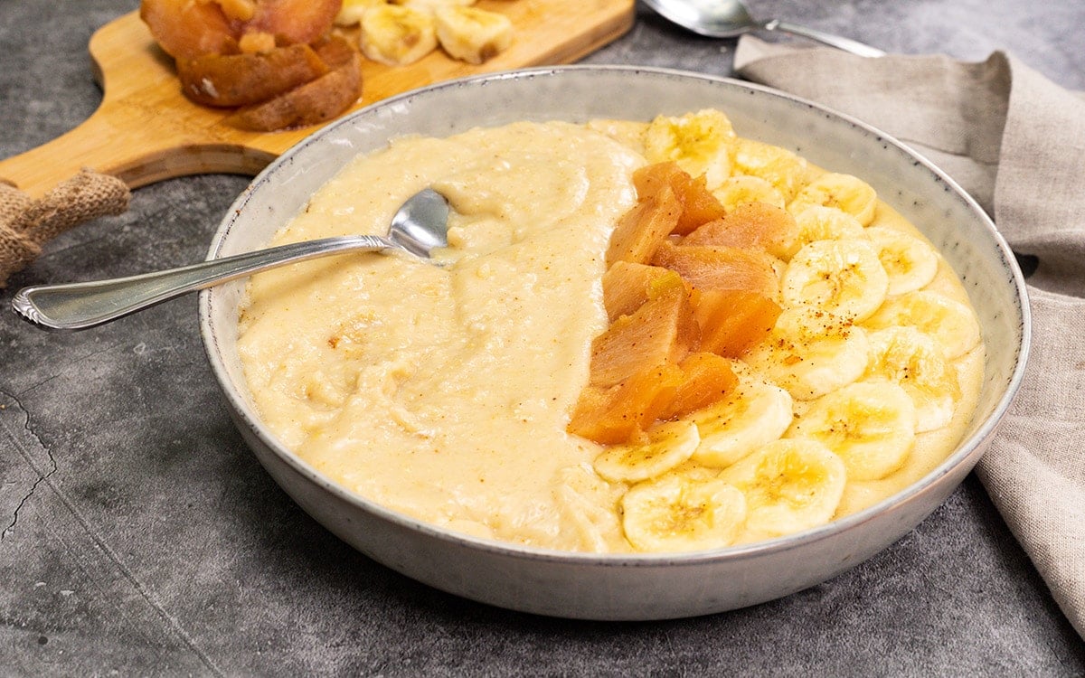 vegan cornmeal porridge in a beige bowl garnished with naseberry and banana slices on a grey background