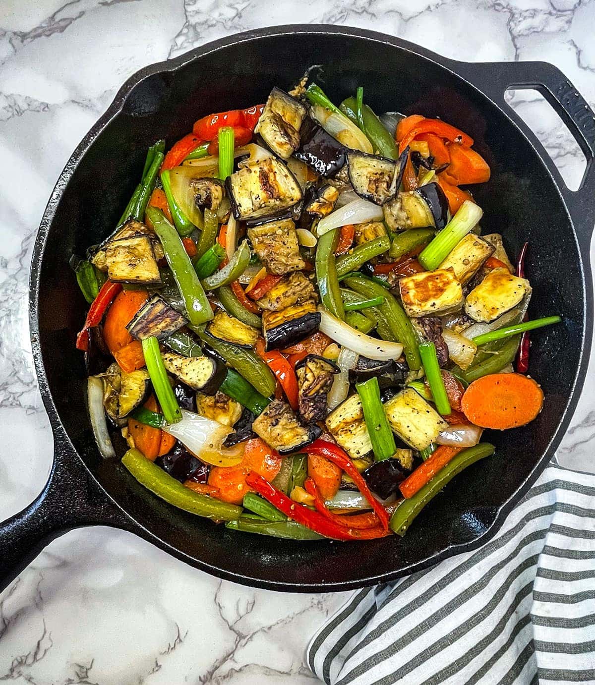eggplant stir fry on black pan on white background