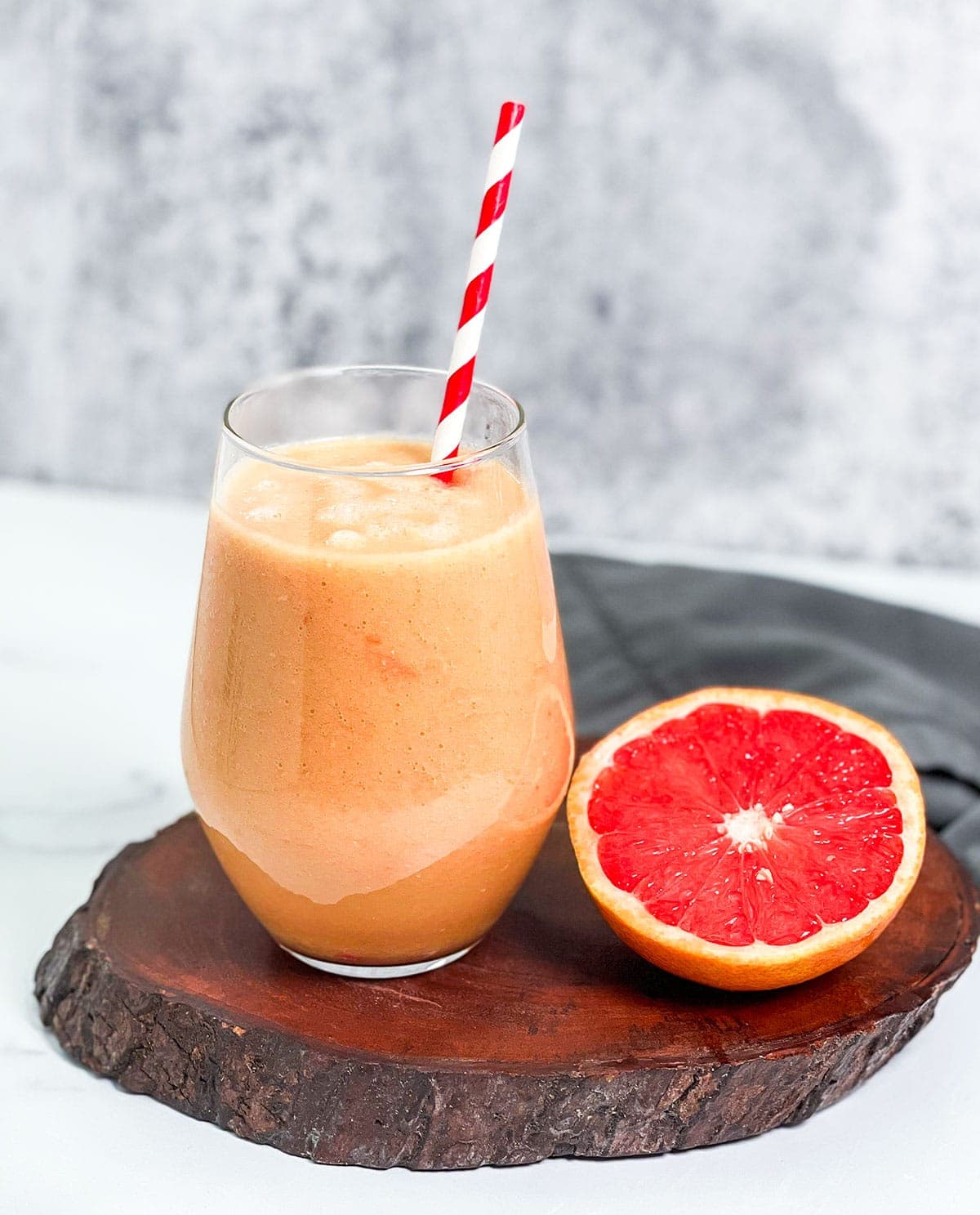 Grapefruit smoothie in a glass on a wooden board with a red and white straw
