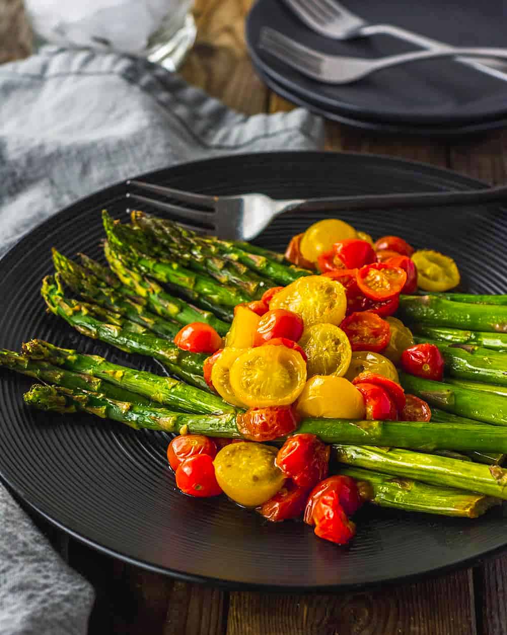 Oven Roasted Asparagus and Tomatoes in black plate wooden background