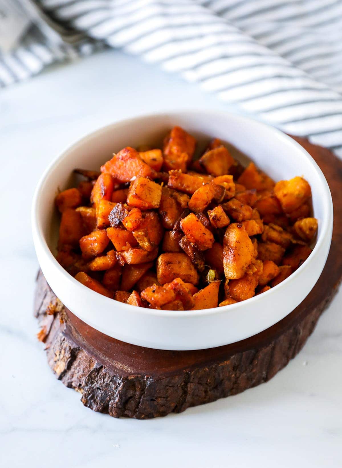 Skillet Sweet Potatoes in a white bowl on a wooden platform