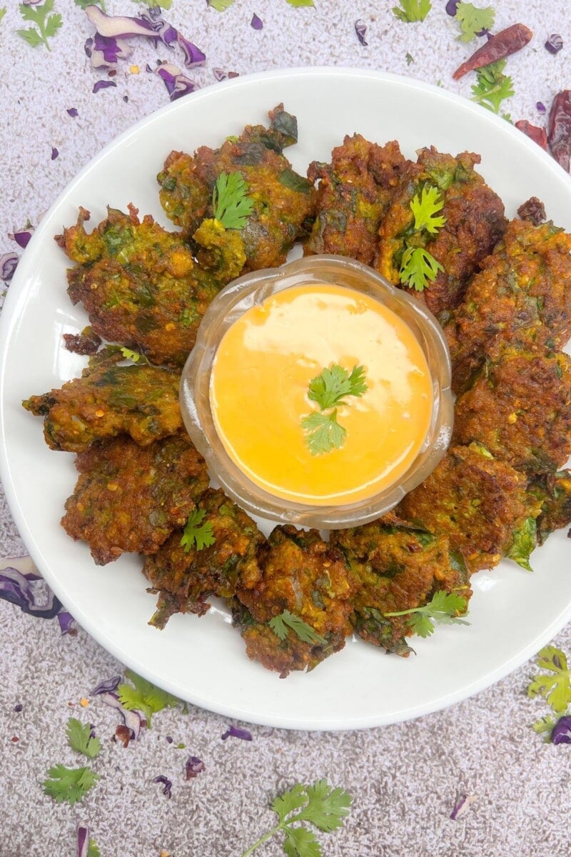 Spinach and yellow lentil bhajis on a white plate on a grey background