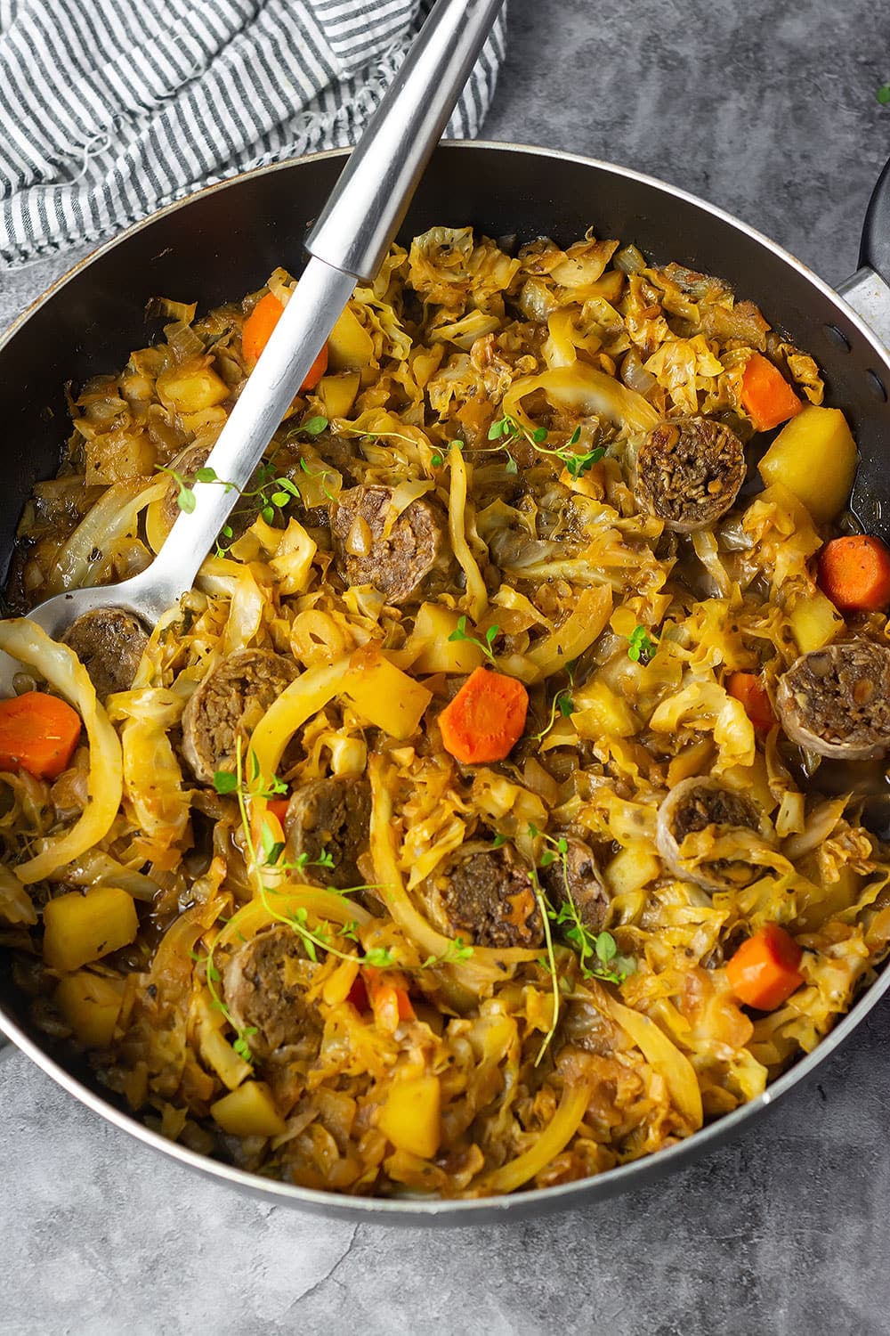 Vegan cabbage, sausage, carrot, potato cooked with creole seasoning and italian seasoning in a skillet on marble background