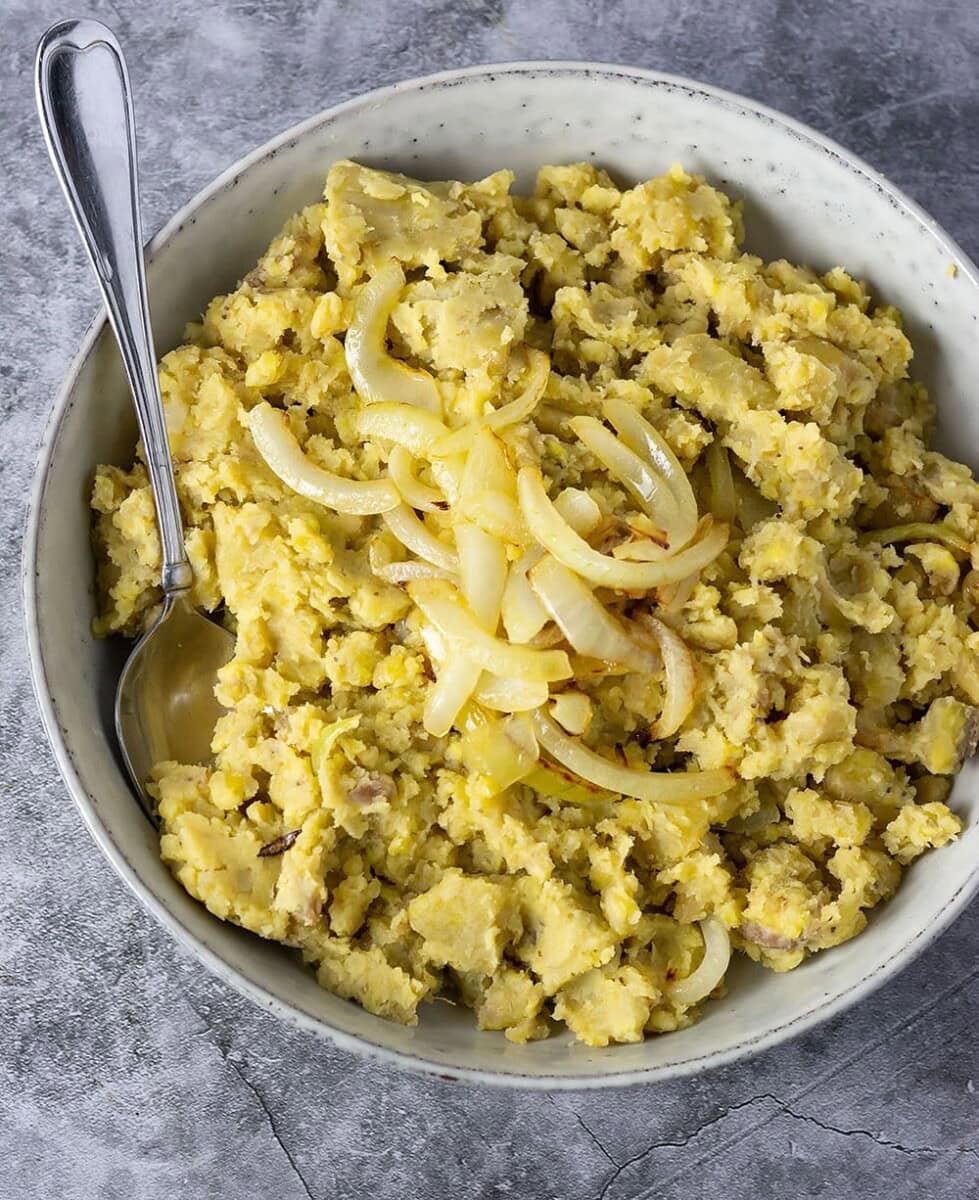 Mangu recipe dominican mashed plantains in a wooden bowl on a wooden cutting board with lime slices on a marbled background overlay