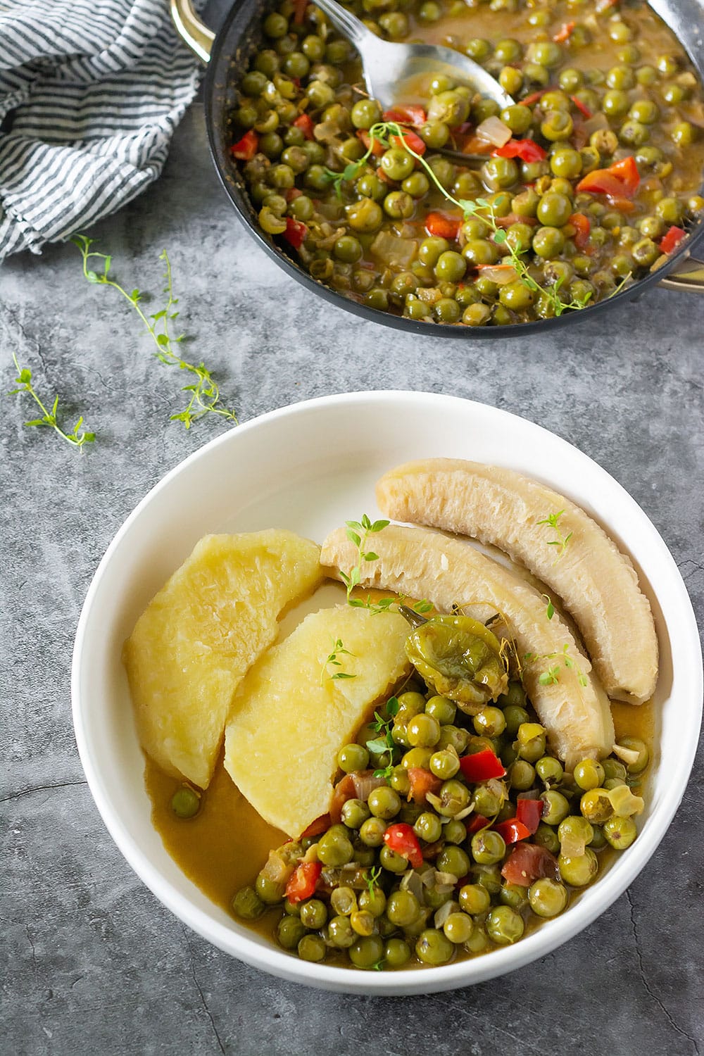 Overlay susumber stew with yellow yam, green banana, in a white bowl with more susuber in a black saucepan in the background