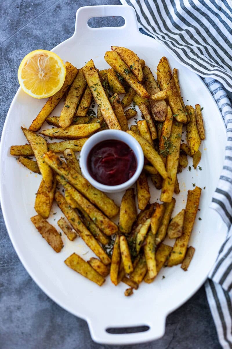 overlay of yam fries on a white platter with lemon, tomato ketchup on a grey background with a black and white napkin