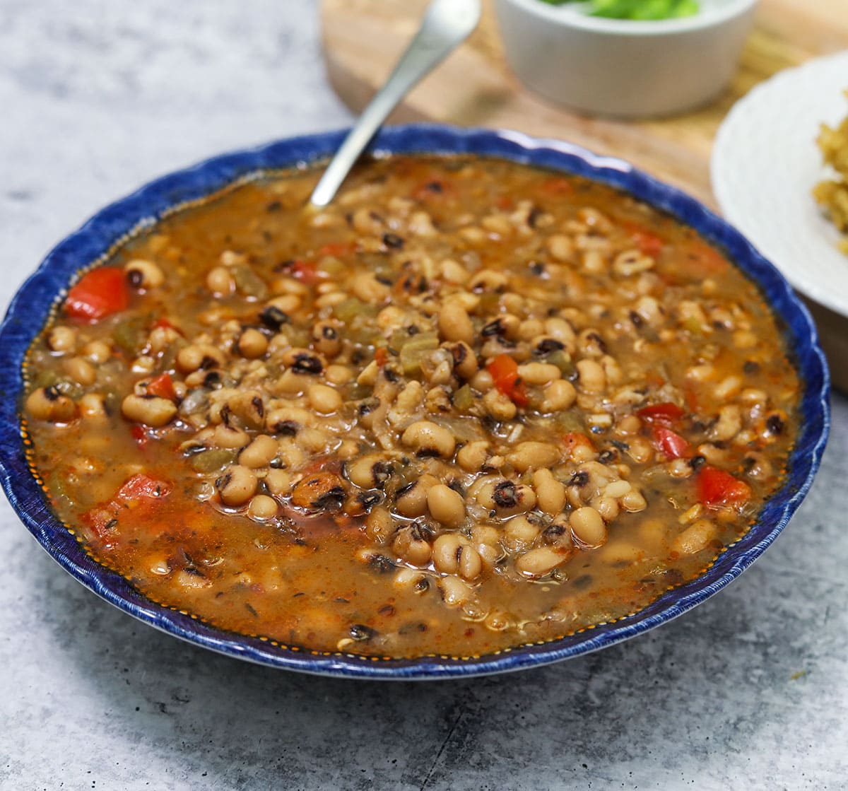 Instant Pot Black Eyed Peas in a blue bowl on a white concrete background with cornbread in the background
