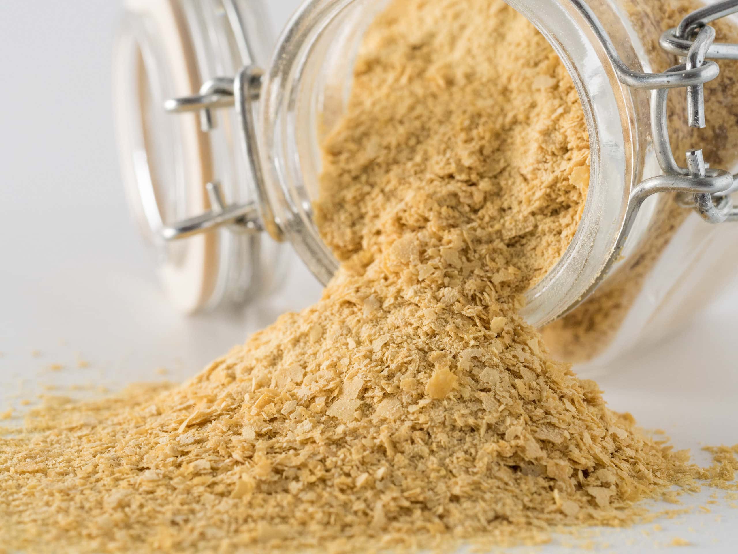 non-fortified nutritional yeast on a glass jar on the side on a white background