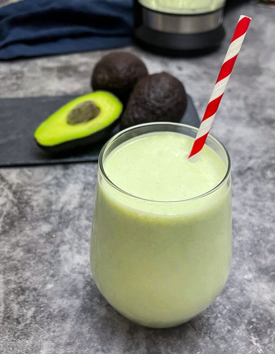 avocado milk in a glass with a red and white stripe straw