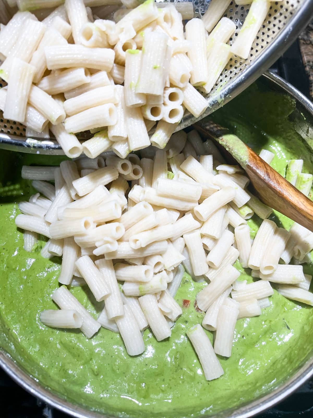 penne pasta being poured in saucepan with pesto sauce