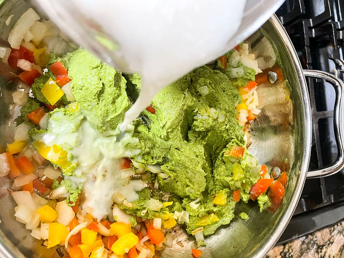 pouring coconut milk in pesto pasta