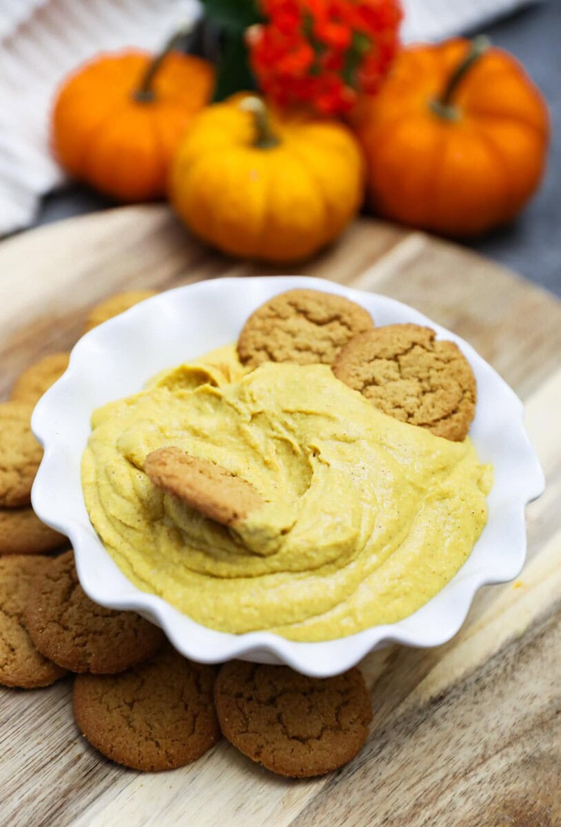 pumpkin hummus in a white bowl on wooden cutting board