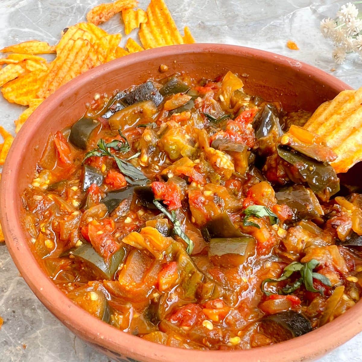 eggplant and tomato chutney in a clay bowl on a white background