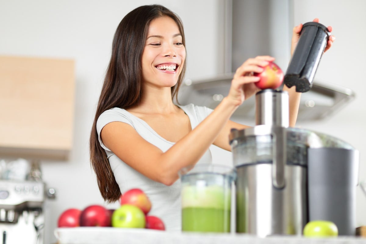 Juicing - woman making apple and green vegetable juice using juicer machine at home in kitchen.