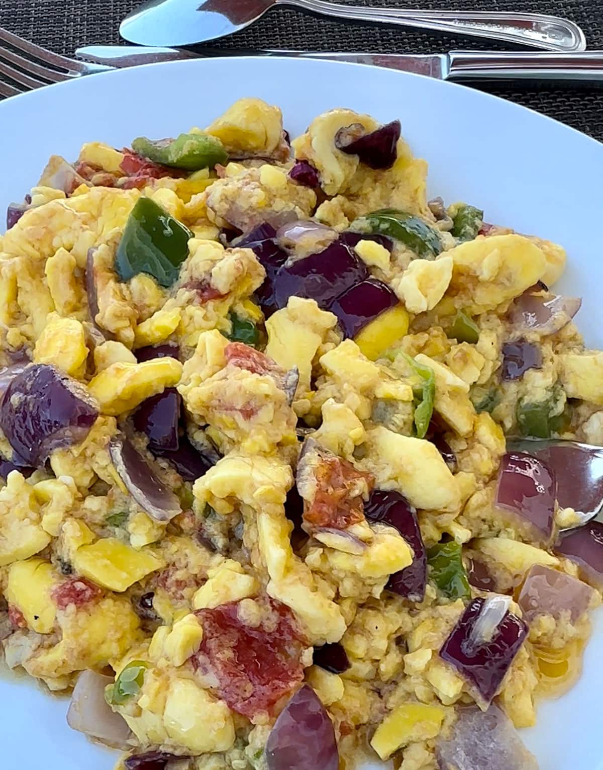 ackee recipe is a staple in Jamaican kitchen, with onions and peppers on a white pepper with knife and fork in the background