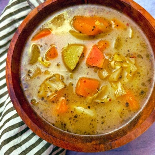 butternut squash and chayote soup in a wooden bowl on a grey background with a black and white napkin