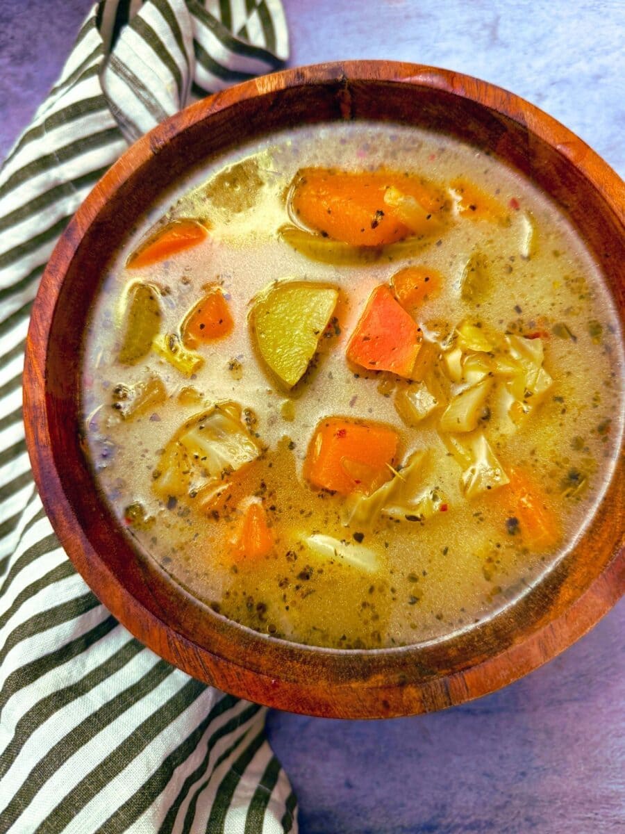butternut squash and chayote soup in a wooden bowl on a grey background with a black and white napkin